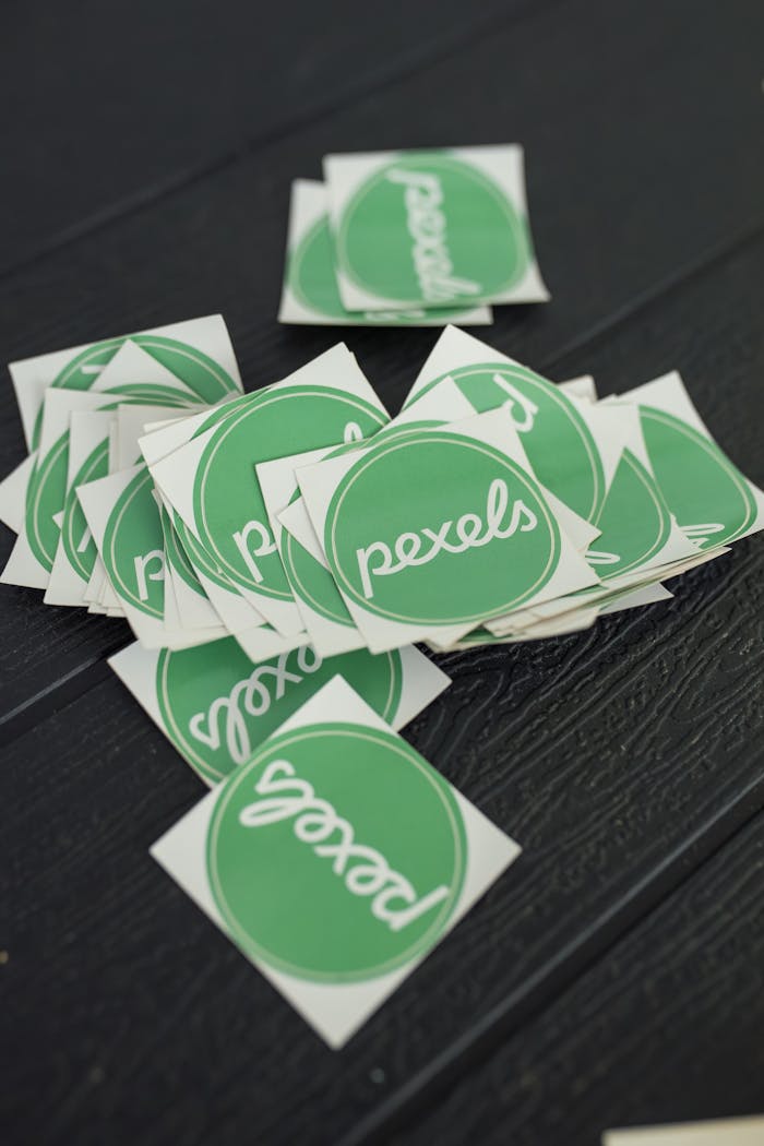 A scattered pile of green Pexels logo stickers on a textured dark surface, perfect for branding visuals.